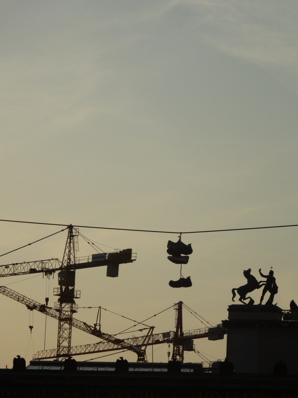 En marchant dans Berlin au crépuscule, paysage étrange avec entrelacs de grues, statues d&rsquo;aigles,de cheval cabré,et deux paires  de chaussures accrochées à un&nbsp;fil.