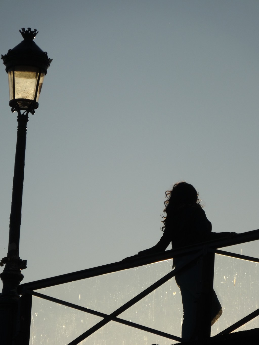 Longeant la Seine au couchant, silhouettes sur un pont semblant aller l&rsquo;une vers&nbsp;l&rsquo;autre.