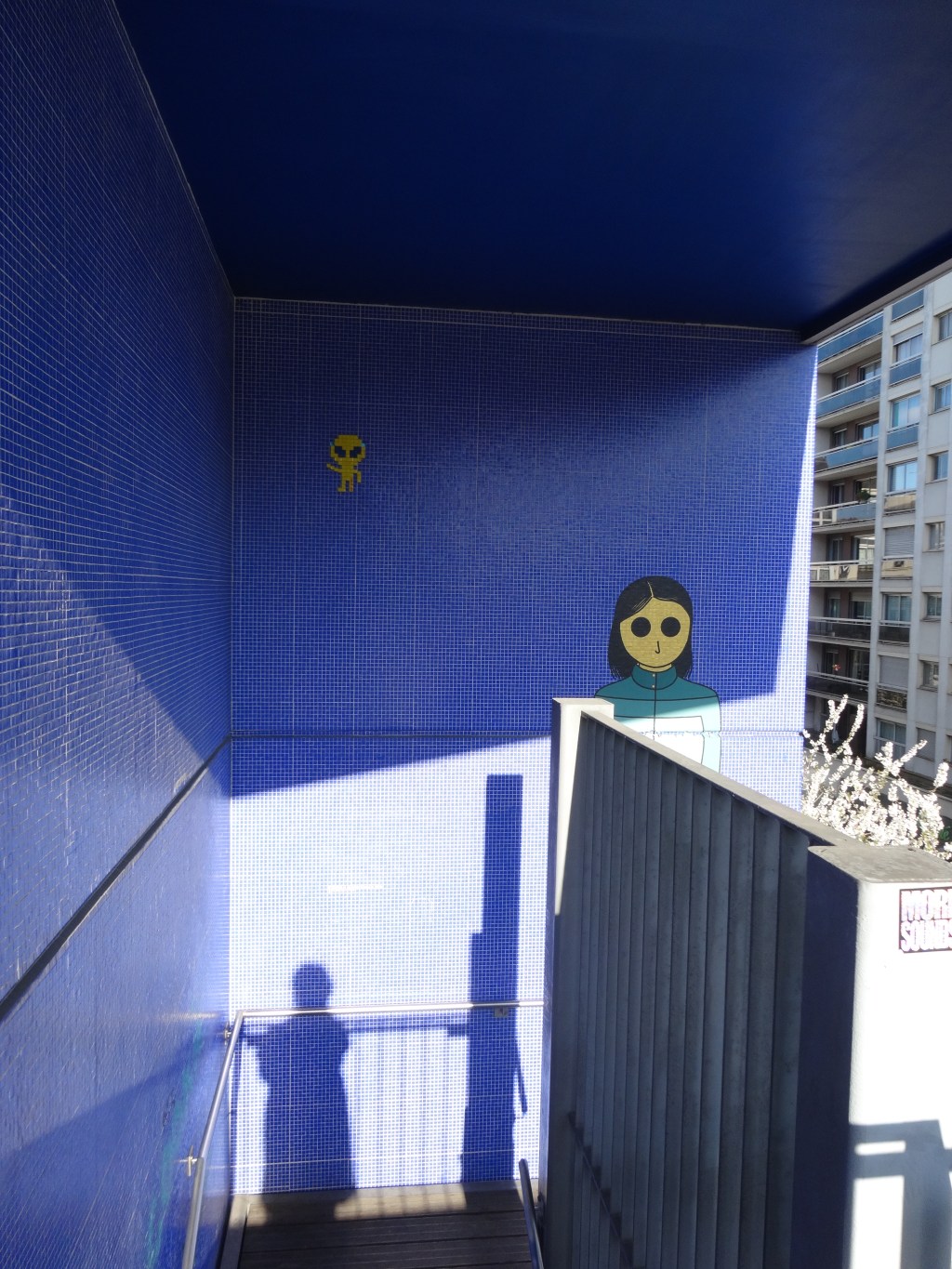 En descendant les marches de la Coulée verte, mon ombre portée sur un mur bleu sous deux regards&nbsp;noirs.